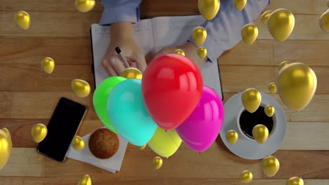 Animation-of-balloons-over-caucasian-woman-writing-and-smartphone