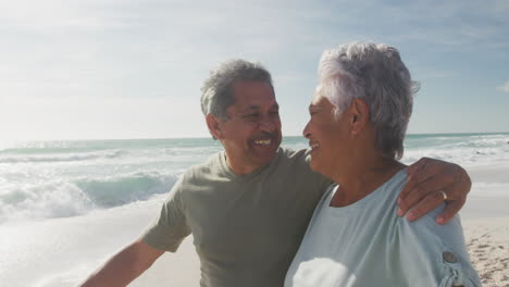 Glückliches-Hispanisches-älteres-Paar,-Das-Sich-Umarmt-Und-Bei-Sonnenuntergang-Am-Strand-Spaziert