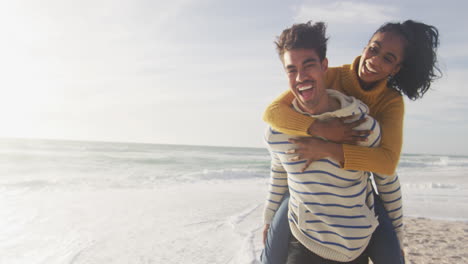 Happy-hispanic-man-carrying-piggyback-woman-and-having-fun-on-beach