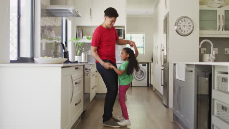 Happy-biracial-father-and-daughter-dancing-in-kitchen-together
