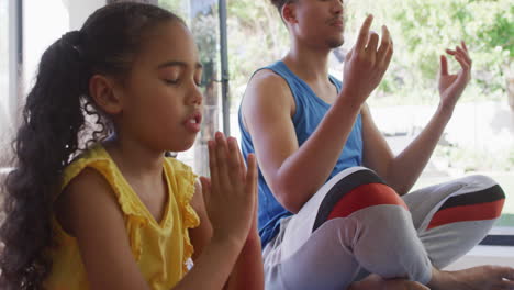 Happy-biracial-father-and-daughter-doing-yoga,-meditating-together