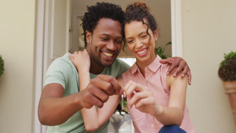 Happy-biracial-couple-embracing-with-joy-and-holding-keys-in-front-of-new-house