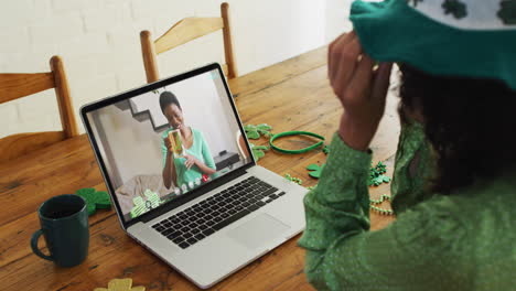 Mujer-Afroamericana-Sonriente-Con-Cerveza-Usando-Una-Banda-En-Forma-De-Trébol-En-Videollamada-En-Una-Computadora-Portátil