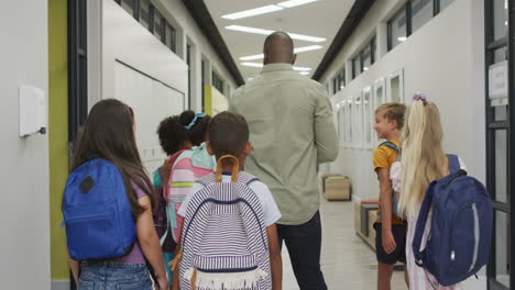 Video-Vom-Rücken-Eines-Afroamerikanischen-Männlichen-Lehrers-Und-Verschiedener-Schüler,-Die-Durch-Die-Schulhalle-Gehen
