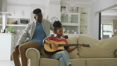 Vídeo-De-Una-Feliz-Pareja-Afroamericana-Sentada-En-El-Sofá,-Cantando-Y-Tocando-La-Guitarra