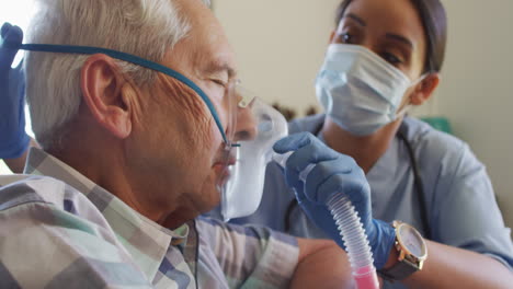 Video-Einer-Birazialen-Ärztin-Mit-Gesichtsmaske,-Die-Einem-Kaukasischen-älteren-Mann-Sauerstoff-Liefert