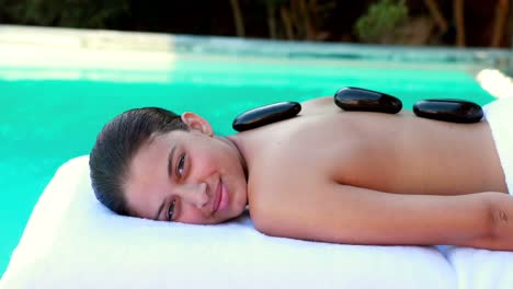 Friedliche-Brünette-Bekommt-Eine-Hot-Stone-Massage-Am-Pool