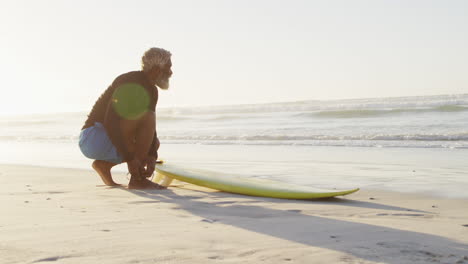 Senior-african-american-man-preparing-before-surfing-on-sunny-beach