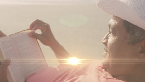 Animation-of-light-spots-over-biracial-man-reading-at-beach