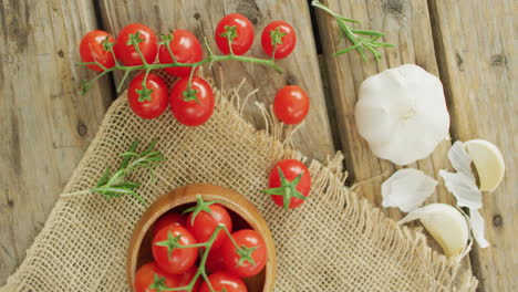 Video-of-fresh-cherry-tomatoes-in-bowl-and-garlic-on-rustic-cloth-over-wooden-background