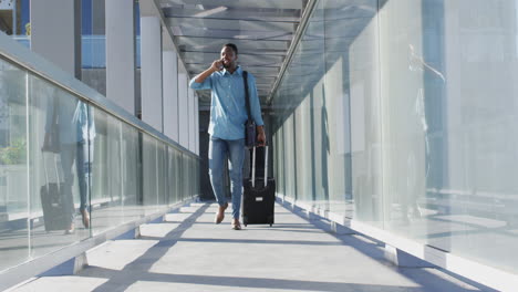 Video-of-african-american-man-walking-with-suitcase-and-using-smartphone