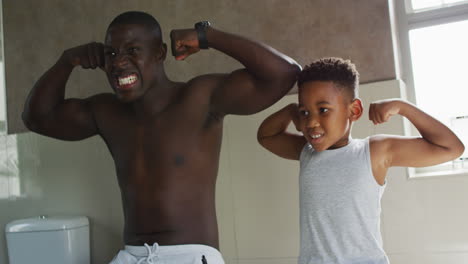 Video-of-happy-african-american-father-and-son-showing-muscles-in-mirror