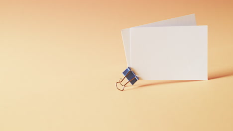 Two-blank-white-business-cards-with-bulldog-clip-on-orange-background,-copy-space,-slow-motion