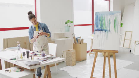 Video-of-biracial-female-artist-preparing-paints-and-working-in-studio