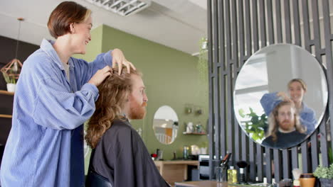 Glückliche-Kaukasische-Friseurin-Berät-Männlichen-Kunden-Mit-Langen-Haaren-Im-Salon,-In-Zeitlupe