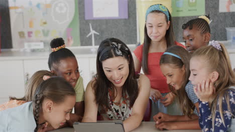 Happy-diverse-female-teacher-with-schoolgirls-using-tablet-in-classroom-at-elementary-school