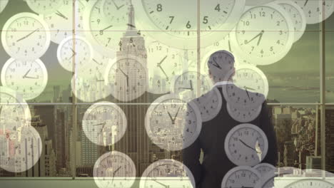 Animation-Fallender-Uhren-über-Der-Rückansicht-Eines-Geschäftsmannes,-Der-Durch-Ein-Glasfenster-Auf-Die-Moderne-Stadt-Blickt