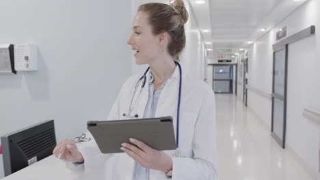 Diverse-female-doctor-and-nurse-using-tablet-and-discussing-at-hospital-reception,-in-slow-motion