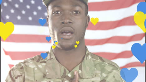 Animation-of-yellow-and-blue-hearts-over-african-american-male-soldier-singing-anthem-on-usa-flag