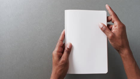 Close-up-of-hand-holding-book-with-copy-space-on-gray-background-in-slow-motion