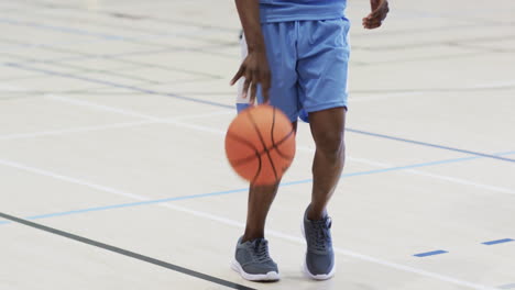 Mittelteil-Eines-Afroamerikanischen-Männlichen-Basketballspielers,-Der-Auf-Dem-Hallenplatz-Einen-Ball-Hüpft,-Zeitlupe