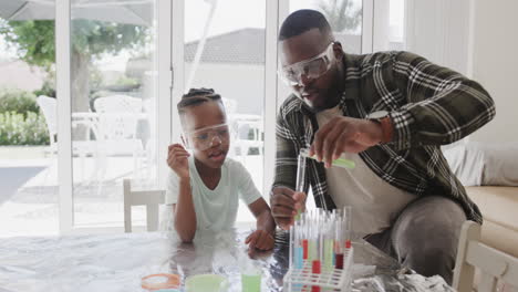African-american-father-and-son-sitting-at-table-holding-test-tubes-with-liquid,-in-slow-motion