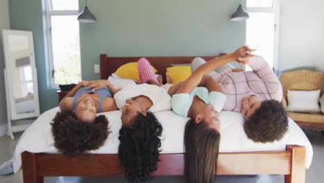 Happy-diverse-female-friends-lying-on-bed-and-smiling-in-bedroom