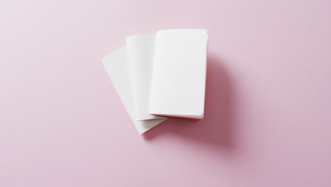 Hand-holding-piece-of-paper-over-pieces-of-paper-with-copy-space-on-pink-background-in-slow-motion