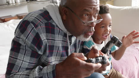 African-american-grandfather-and-grandson-sitting-on-sofa-and-playing-video-games,-slow-motion