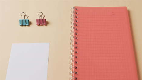 Close-up-of-red-notebook-and-school-stationery-arranged-on-beige-background,-in-slow-motion