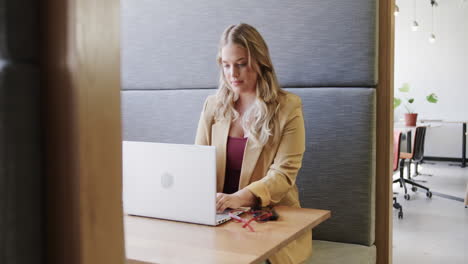 Portrait-of-happy-plus-size-caucasian-casual-businesswoman-using-laptop-at-office-lounge