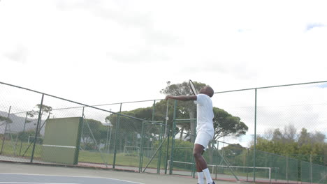 Afroamerikanischer-Männlicher-Tennisspieler,-Der-In-Zeitlupe-Den-Ball-Auf-Dem-Tennisplatz-Im-Freien-Serviert