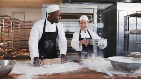 Happy-diverse-female-and-male-bakers-working-in-bakery-kitchen,-rolling-out-dough,-slow-motion