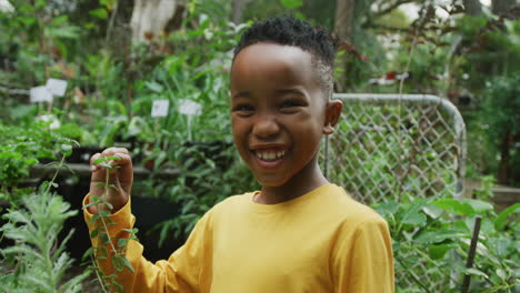 Portrait-of-happy-african-american-boy-looking-at-plants-and-smiling-in-garden
