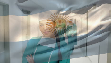 Animation-of-argentinian-flag,-biracial-female-surgeon-standing-arms-crossed-in-corridor-of-hospital