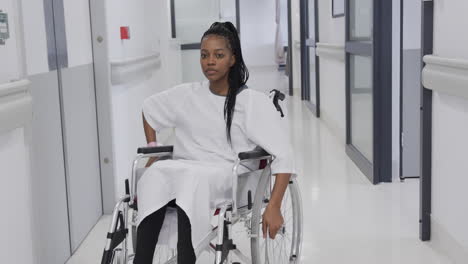 African-american-female-patient-in-wheelchair-in-hospital-corridor,-slow-motion