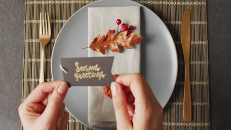Video-of-hands-putting-card-with-greeting-on-plate-with-autumn-decoration-lying-on-wooden-mat