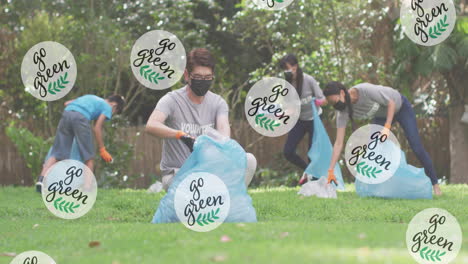 Animation-of-leaves-and-go-green-text-over-diverse-volunteers-collecting-plastics-in-bags-at-park