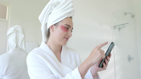Glückliche-Kaukasische-Frau,-Die-Augenklappen-Trägt-Und-Ihr-Smartphone-Im-Badezimmer-In-Zeitlupe-Benutzt