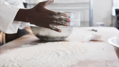Diverse-bakers-working-in-bakery-kitchen,-pouring-flour-on-counter-in-slow-motion