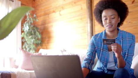 Happy-african-american-woman-using-laptop-and-credit-card-in-living-room,-in-slow-motion