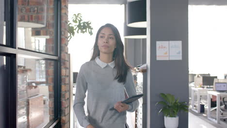 Biracial-casual-businesswoman-walking-through-office-with-tablet,-slow-motion