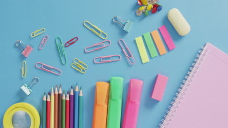 Video-of-various-office-supplies,-pens,-paper-clips,-pins-on-blue-background