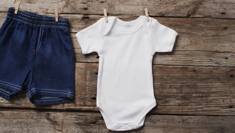 Video-of-baby-grow-and-denim-shorts-hanging-on-clothes-pegs-with-copy-space-on-wooden-background