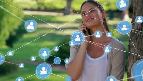 Animation-of-network-of-profile-icons-over-happy-caucasian-woman-talking-on-smartphone-in-the-park