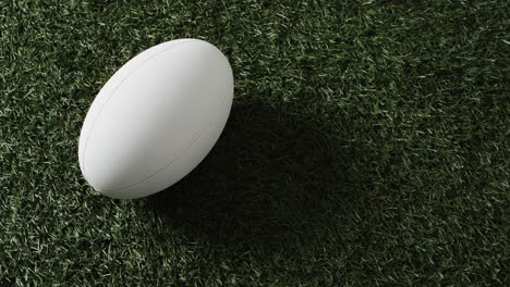 Weißer-Rugbyball-Auf-Sonnenbeschienenem-Gras-Mit-Kopierraum,-Zeitlupe