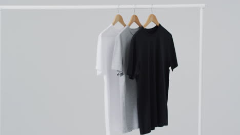 Video-Von-Weißen,-Grauen,-Schwarzen-T-Shirts-Auf-Kleiderbügeln-Und-Kopierraum-Auf-Weißem-Hintergrund