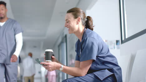 Caucasian-female-doctor-using-smartphone-and-drinking-coffee-in-corridor,-copy-space,-slow-motion