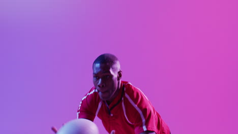 African-american-male-rugby-player-catching-rugby-ball-over-pink-lighting
