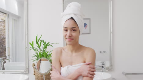 Portrait-of-biracial-woman-with-towel-smiling-in-bathroom